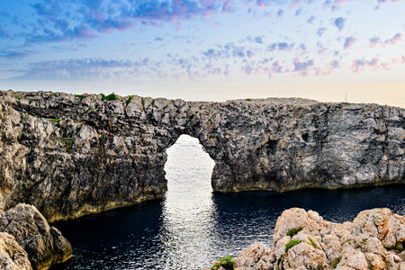 Spectacular sunset at Pont d'en Gil â Cala Corbetar in Ciutadella, Menorca, Balearic Islands. Peculiar natural formation in the form of an archの写真素材