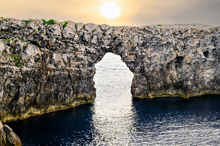 Spectacular sunset at Pont d'en Gil â Cala Corbetar in Ciutadella, Menorca, Balearic Islands. Peculiar natural formation in the form of an archの写真素材