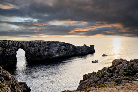 Spectacular sunset at Pont d'en Gil â Cala Corbetar in Ciutadella, Menorca, Balearic Islands. Peculiar natural formation in the form of an archの写真素材