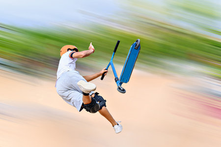 Young man practicing Scootering (Freestyle Scootering) in the SkatePark in the central park of...