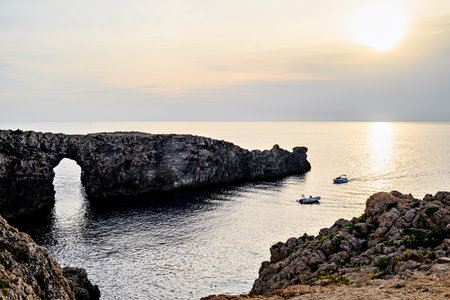 Spectacular sunset at Pont d'en Gil â Cala Corbetar in Ciutadella, Menorca, Balearic Islands. Peculiar natural formation in the form of an archの写真素材