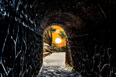 View from inside a tunnel toward a green landscape with trees at sunset.の写真素材