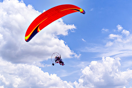 Paragliding adventure with a red and blue parachute on a sunny day.の写真素材