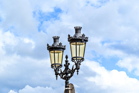 Wrought iron lamppost under a blue sky with white clouds in the Plaza des Born in Ciutadella, Menorcaの写真素材