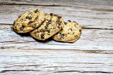 Three chocolate chip cookies isolated on rustic wooden table.