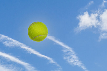 Tennis ball in the air against blue sky and white cloudsの写真素材
