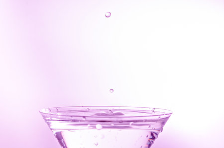 Close-up of water drop falling into a glass on white backgroundの写真素材