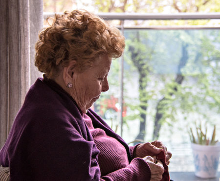 Elderly woman sitting by the window sewingの写真素材