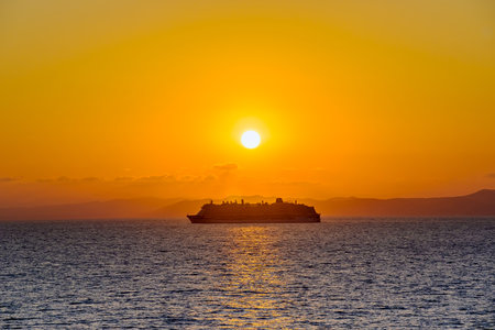 Silhouette of a cruise ship at sea during an orange sunset sky over the horizonの写真素材