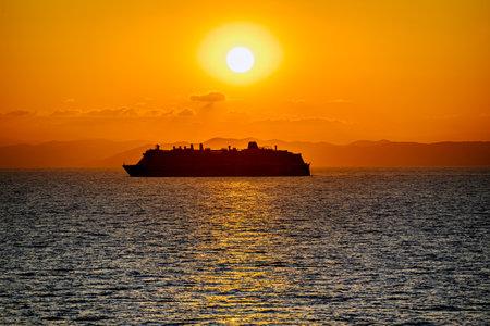 Silhouette of a cruise ship at sea during an orange sunset sky over the horizonの写真素材