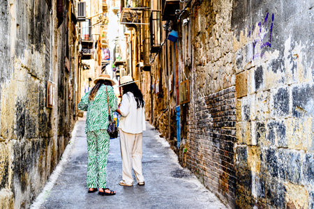 Two tourists stroll down a narrow, typical street in the old town of Palermo, Italy, Sicily.の写真素材