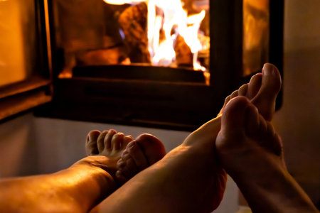 A pair of feet in front of the fireplace. A woman and man warm themselves by the fire.の写真素材