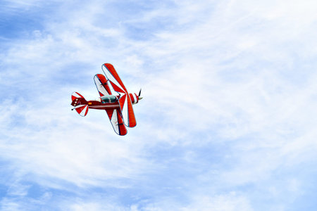 A red aerobatic biplane performing air shows in a blue sky with white clouds. Classic airplanes