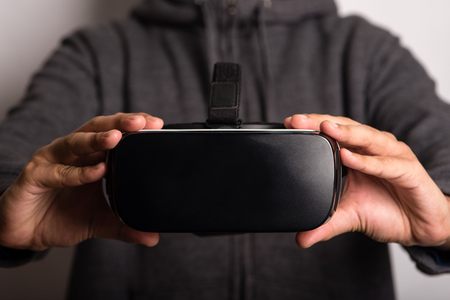 Detail frontal view of virtual reality headset, held by young man, selective focus