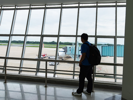 Man looking on the private jet,Asia young man is standing near window at the airport and watching plane before departure. He is standing and carrying luggage. Focus on his back,tourist,tripのeditorial素材