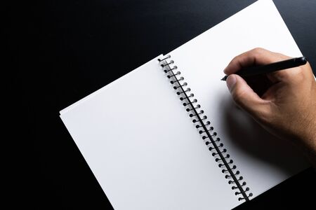 Man hands writing on book in office.Business Man working on desk of black material.