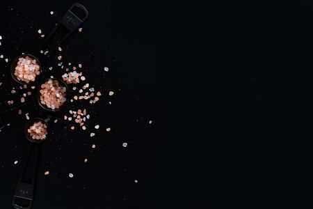 Black measuring spoons with Himalayan salt on black background.の写真素材