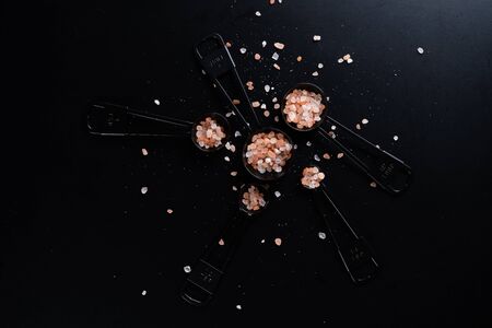 Black measuring spoons with Himalayan salt on black background.の写真素材