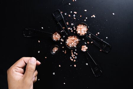 A man hand holding  a measuring spoon with Himalayan salt isolated on Black background.の写真素材