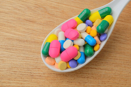 colorful medicine capsule pill on spoon, wood background