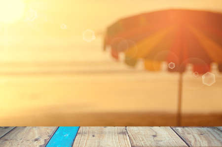 Blur umbrella on tropical sunset beach with old empty wood table background.