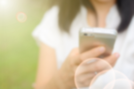 Blur woman use smart phone in hand at green park abstract background.の写真素材