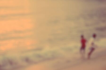 Blur children playing on tropical sunset beach abstract background.Sun light bokeh effect.の写真素材