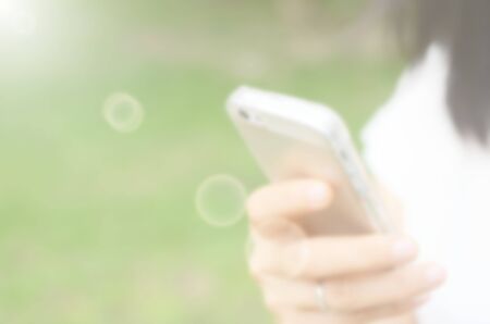 Blur woman use smart phone in hand at green park abstract background.の写真素材
