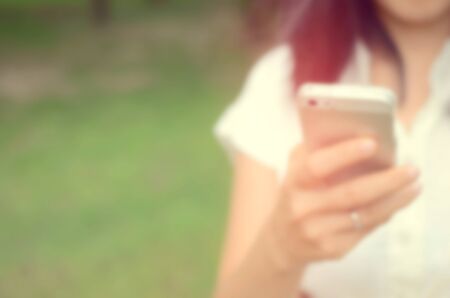 Blur woman use smart phone in hand at green park abstract background.の写真素材