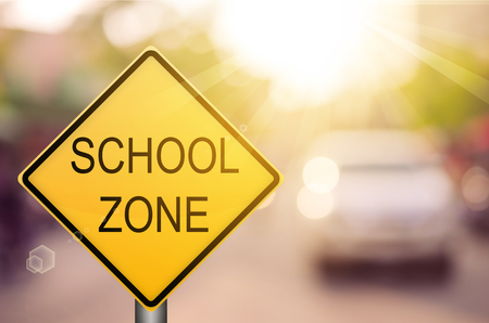 School zone warning sign on blur traffic road with colorful bokeh light abstract background. Copy space of transportation and travel concept. Vintage tone filter color style.の写真素材