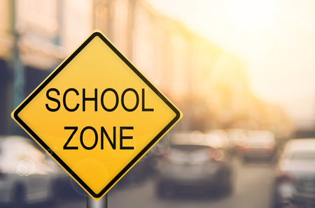 School zone warning sign on blur traffic road with colorful bokeh light abstract background. Copy space of transportation and travel concept. Vintage tone filter color style.の写真素材