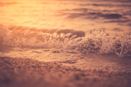 Close up of smooth wave sunset beach and sand texture background. Copy space of summer vacation and travel adventure concept. Shallow depth of field. Vintage tone filter color style.の写真素材