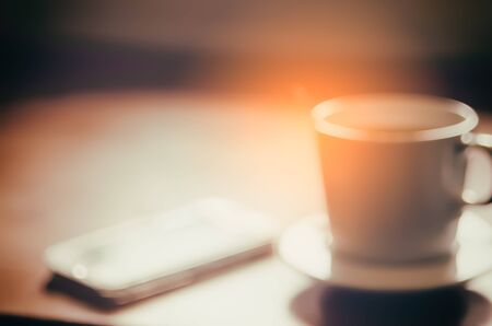 Blur cup of coffee and smart phone abstract background. Copy space of lifestyle and drink concept. Vintage tone filter color style.の写真素材