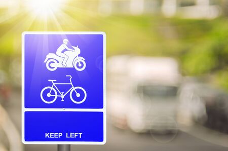 Motorcycle and bicycle keep left lane warning sign on blur traffic road with colorful bokeh light abstract background. Copy space of transportation and travel concept. Retro tone filter color style.の写真素材