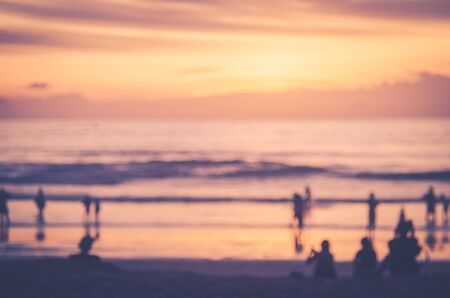 Blur people relax on tropical sunset beach with bokeh sun light wave abstract background. Copy space of summer vacation and business travel concept. Vintage tone filter color style.の写真素材