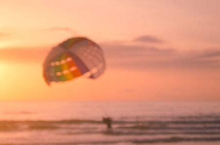 Blur people relax on tropical sunset beach with parachuting boat abstract background.Travel concept.Retro color style.の写真素材