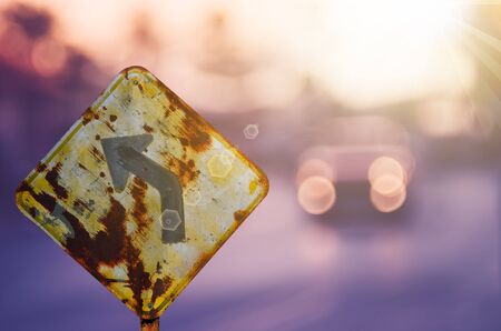 Old curve road warning sign on blur traffic road with colorful bokeh light abstract background. Copy space of transportation and travel concept. Retro tone filter color style.の写真素材