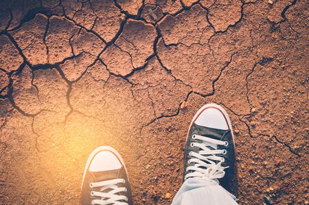 Top view of shoes and blue jean on dry crack soil texture background, selfie. Copy space of fashion and travel adventure concept. Vintage tone color style.の写真素材