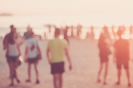 Blur people relax on tropical sunset beach with bokeh sun light wave abstract background. Copy space of summer vacation and business travel concept. Vintage tone filter color style.の写真素材