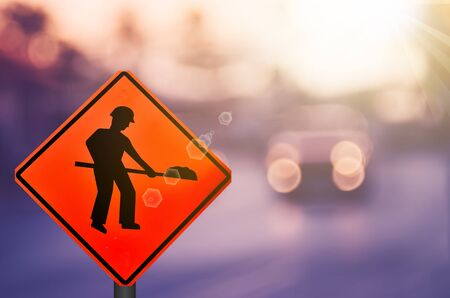 Construction warning sign on blur traffic road with colorful bokeh light abstract background. Copy space of transportation and travel concept. Retro tone filter color style.の写真素材