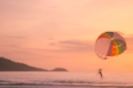 Blur people relax on tropical sunset beach with parachuting boat abstract background.Travel concept.Retro color style.の写真素材