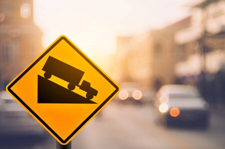 Down hill warning sign on blur traffic road with colorful bokeh light abstract background. Copy space of transportation and travel concept. Retro tone filter color style.の写真素材
