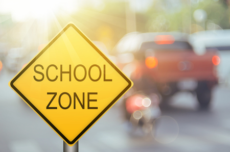 School zone warning sign on blur traffic road with colorful bokeh light abstract background. Copy space of transportation and travel concept. Vintage tone filter color style.