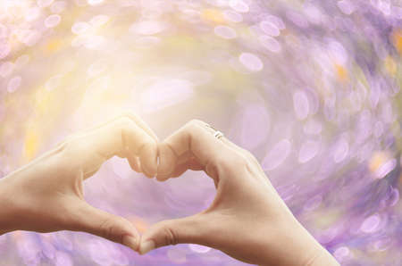 Female hands heart shape on nature pink bokeh sun light flare and blur leaf abstract background....