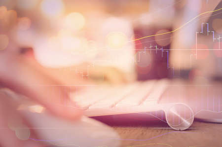 Business economic and technology working concept. Woman hand using keyboard double expose with graph money stock trading and blur people bokeh light background. Vintage tone filter effect color style.の写真素材