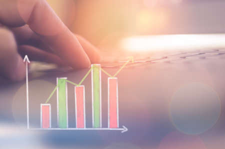 Business economic and technology working concept. Man hand using notebook double exposure with graph money stock trading and blur bokeh light background. Vintage tone filter effect color style.の写真素材