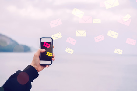 Woman hand using smart phone double exposure email fly draw bokeh at beach .Business economic technology working connect and travel adventure summer holiday concept. Vintage tone filter color style.の写真素材