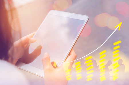 Business economic technology working concept. Woman using smart phone tablet street double exposure graph money stock trading up trend arrow bar bokeh people background.Vintage tone filter effect color styleの写真素材