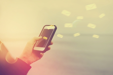 Woman hand using smart phone double exposure email fly draw bokeh at beach .Business economic technology working connect and travel adventure summer holiday concept. Vintage tone filter color style.の写真素材