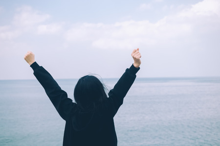Freedom feel good and travel adventure concept. Copy space of silhouette woman rising hands with blue sky and white cloud on beach background. Vintage tone filter effect color style.の写真素材